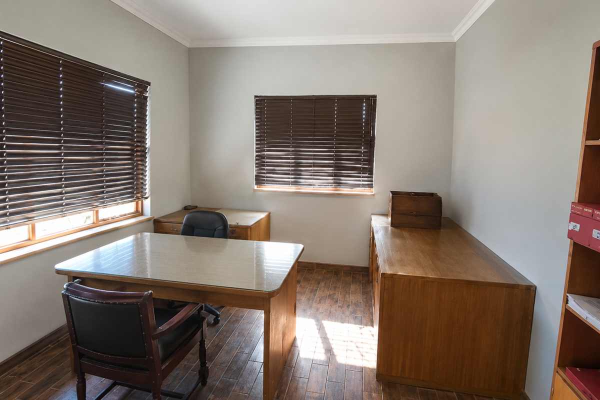 A well-maintained office space featuring timber-look flooring, crown molding, and dual windows fitted with venetian blinds, providing a professional and functional work environment.