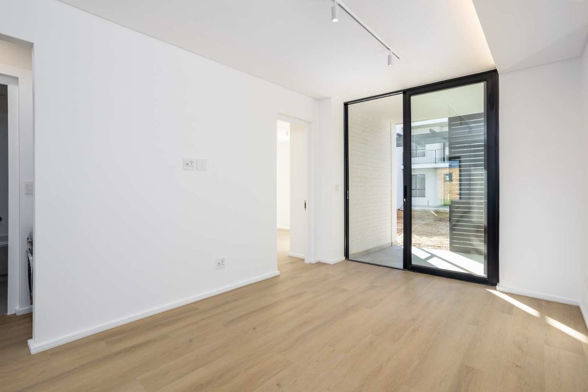 A bright, modern living area featuring light wood-look flooring, recessed track lighting, and large sliding glass doors opening to an outdoor patio space.