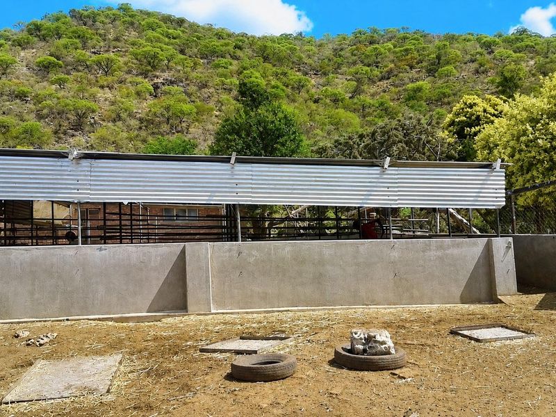 An outdoor livestock or utility area featuring a concrete boundary wall and corrugated metal fencing set against a natural hillside backdrop.