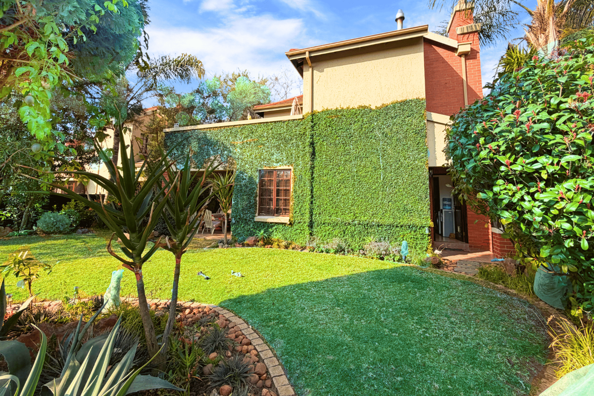 A view of the rear garden featuring a lush, creeper-covered brick facade, a well-maintained lawn with stone edging, and a prominent chimney.