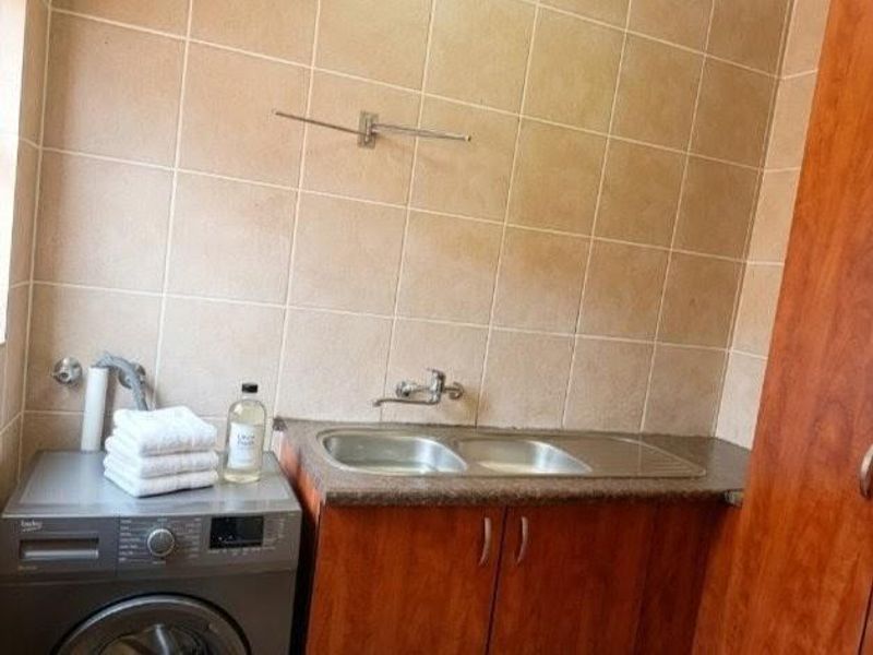 Functional laundry area featuring a double stainless steel sink, laminate countertop, and wooden cabinetry with tiled splashback.