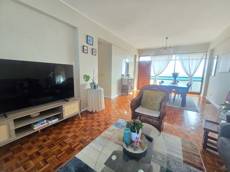 Open-plan living and dining area featuring classic parquet flooring and large sliding glass doors leading to a balcony with natural light.
