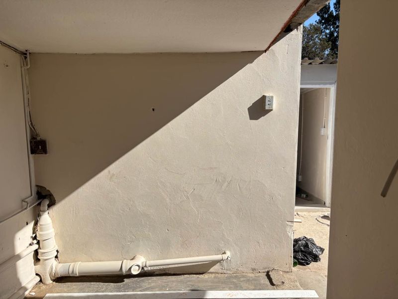 An outdoor utility area featuring exposed plumbing and electrical infrastructure, showing signs of wear and unfinished wall surfaces.