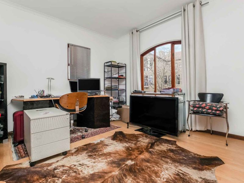 A functional home office space featuring laminate flooring and a large arched window that provides natural light.
