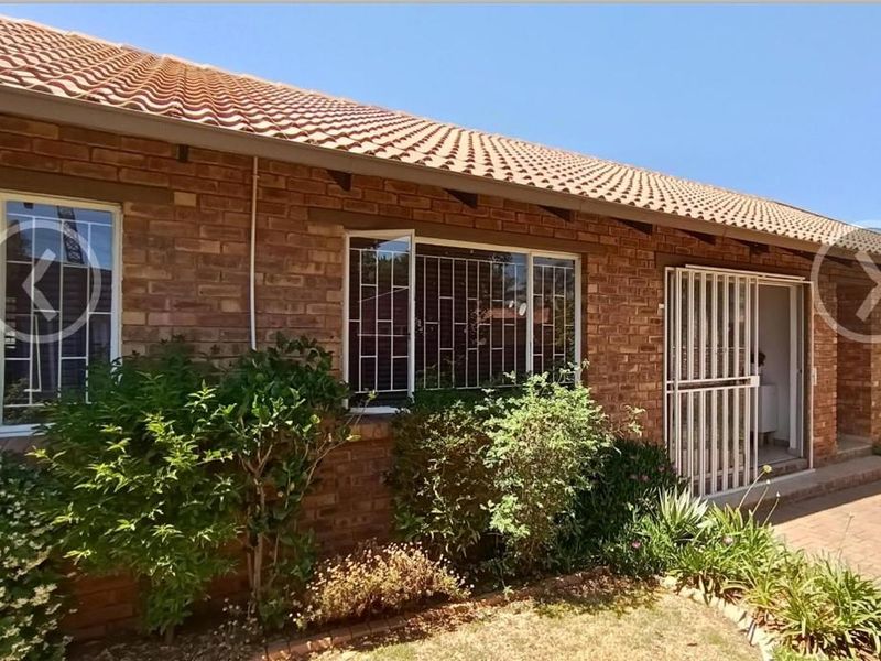Rear exterior view of a face brick townhouse featuring a tiled roof, security bars on windows, and a paved patio area.