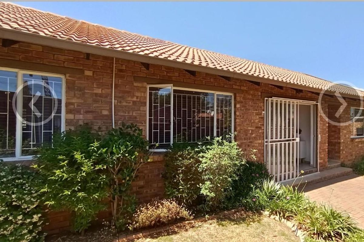 Rear exterior view of a face brick townhouse featuring a tiled roof, security bars on windows, and a paved patio area.