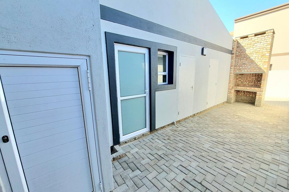 Rear exterior view featuring a paved courtyard, built-in brick braai, and multiple access points to the home with modern finishes.