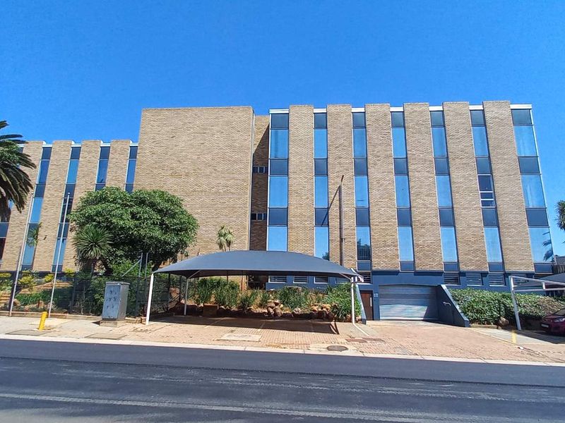 A multi-story office building featuring a brick and glass facade, paved driveway, and covered parking bays.