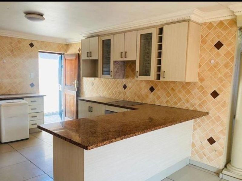 A functional kitchen featuring granite countertops, a breakfast bar, and ample built-in cabinetry with a decorative column and tiled backsplash.