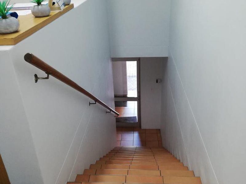 A functional office staircase featuring tiled steps and a wooden handrail, leading down to a glass-panelled exterior entrance door.