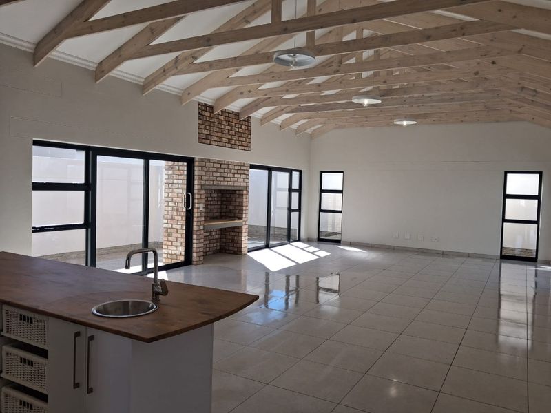 Spacious open-plan living area featuring exposed timber trusses, a brick fireplace, tiled floors, and large aluminium sliding doors leading to the exterior.