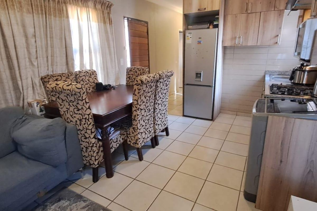 Open plan living and kitchen area featuring tiled flooring, wood-look cabinetry, and a built-in gas hob with extractor fan.