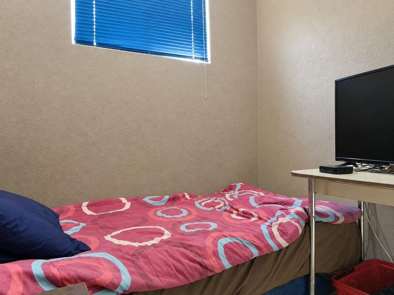 A compact bedroom featuring neutral wall finishes and a window fitted with blue venetian blinds.