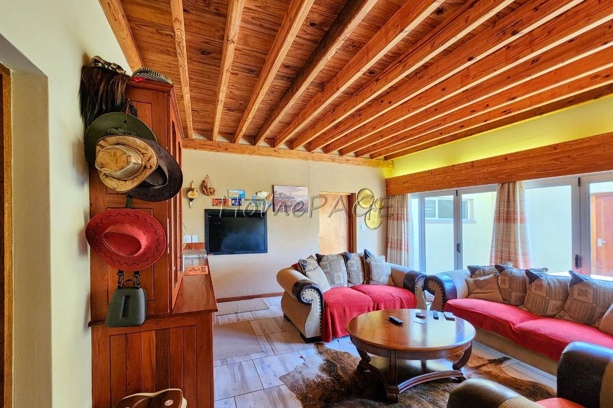 A cozy living room featuring exposed timber beam ceilings, tiled flooring, and large sliding glass doors providing natural light and access to the exterior.
