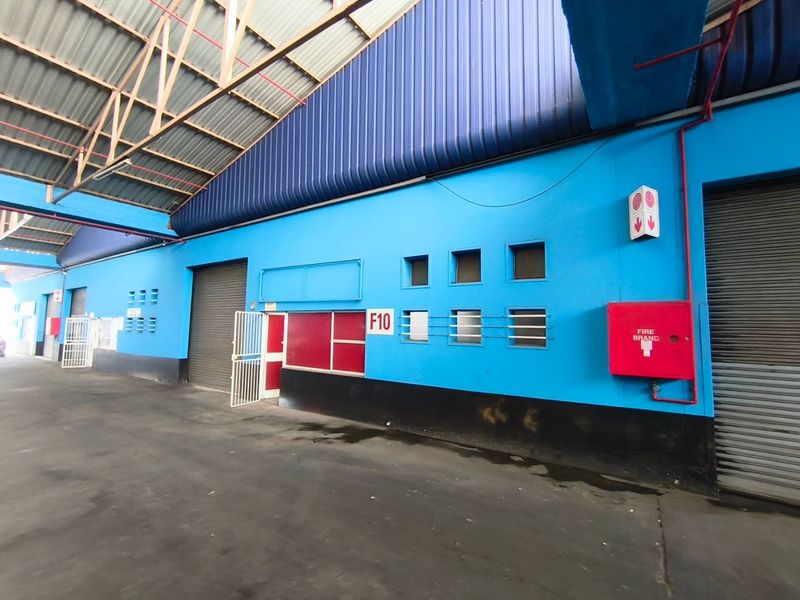 Industrial warehouse corridor featuring high-clearance metal roofing, roller shutter access points, and integrated fire safety equipment.