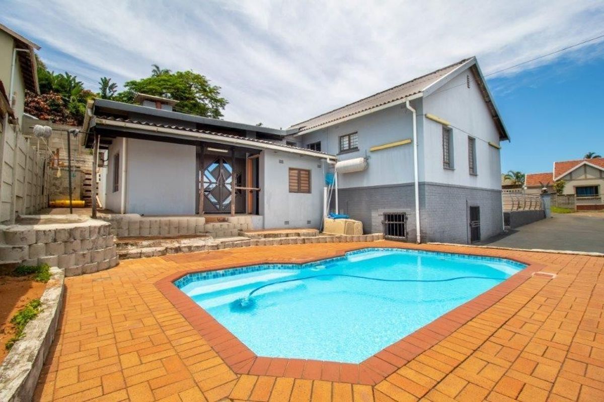 Rear exterior view of the property featuring a swimming pool, paved patio area, and a multi-level garden retaining wall.