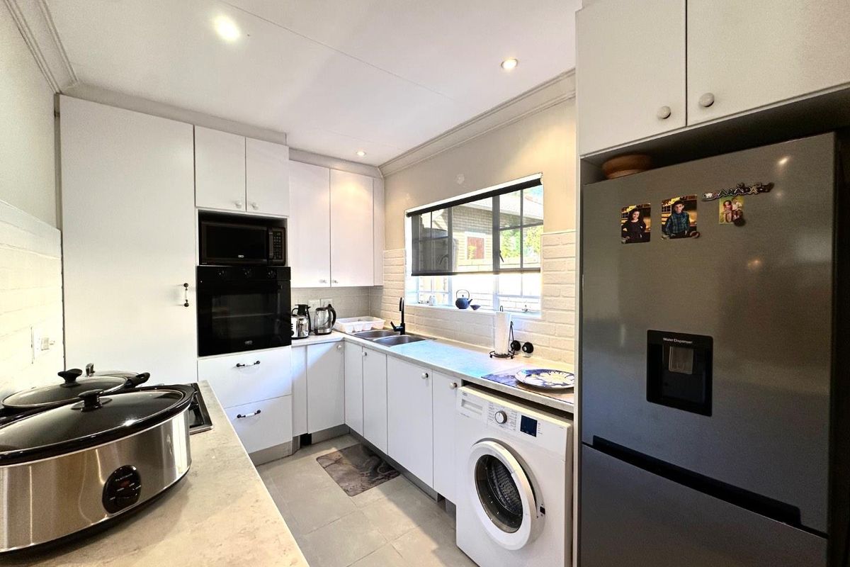 A functional kitchen featuring white cabinetry, built-in oven and microwave, stone-look countertops, and tiled flooring with integrated laundry appliance space.