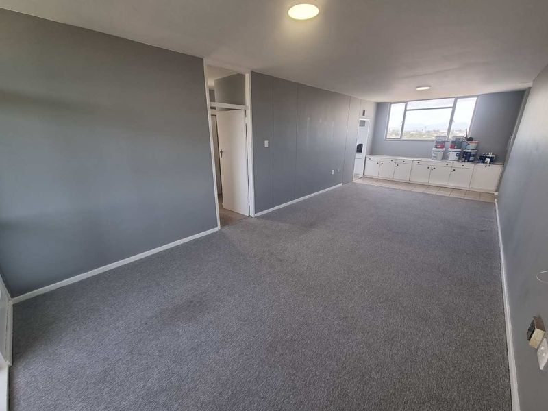 Spacious, empty living area featuring grey carpeting, neutral walls, and built-in storage cabinetry under the window.