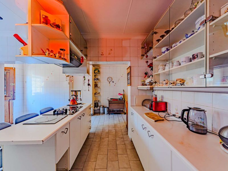 A dated kitchen featuring white cabinetry, tiled splashbacks, and a gas hob, offering a functional layout with potential for modern renovation.
