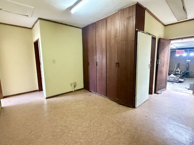 An empty office space featuring built-in wooden cupboards, fluorescent lighting, and vinyl flooring, offering a functional layout for a professional workspace.