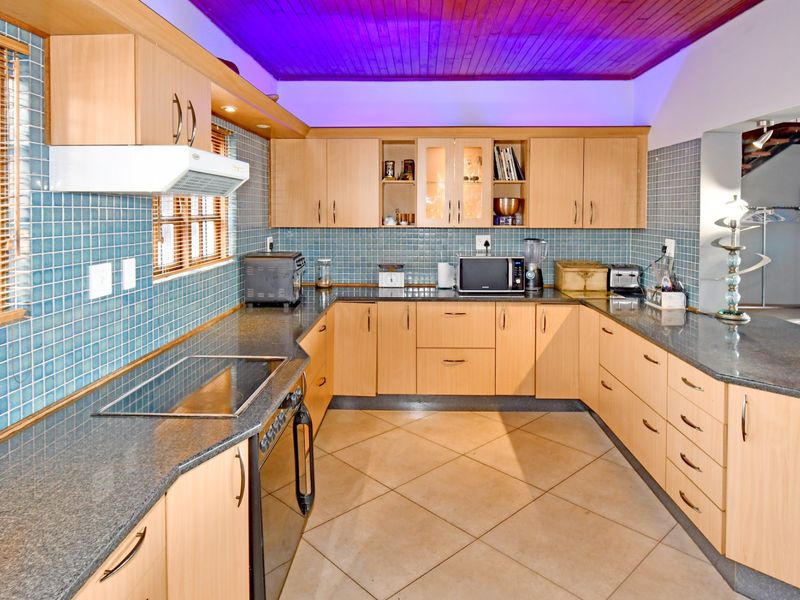 A functional U-shaped kitchen featuring light wood cabinetry, granite countertops, blue tiled backsplash, and a distinctive timber ceiling.