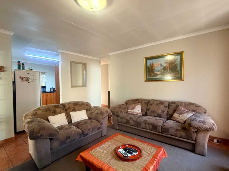 A comfortable living room area featuring neutral wall tones, tiled flooring, and coved cornicing, providing a functional space with direct access to the kitchen area.