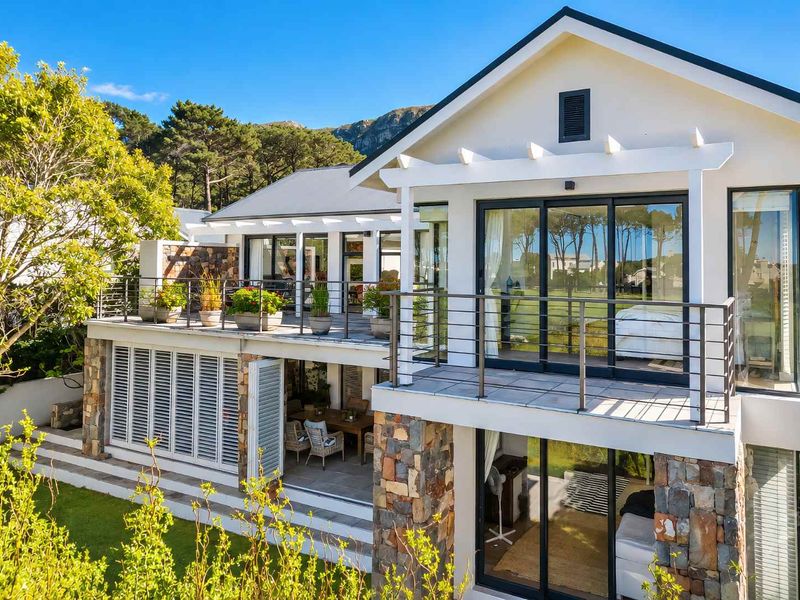 Rear view of a multi-level home featuring stone cladding, a spacious balcony with metal railings, and a covered patio area overlooking the garden.