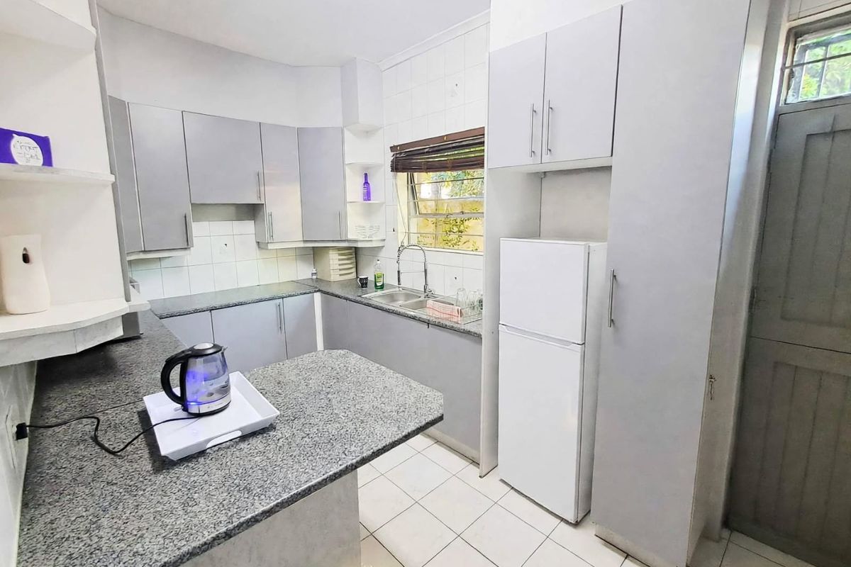 Functional kitchen featuring grey built-in cabinetry, granite countertops, double basin sink, and tiled flooring with a bright window.