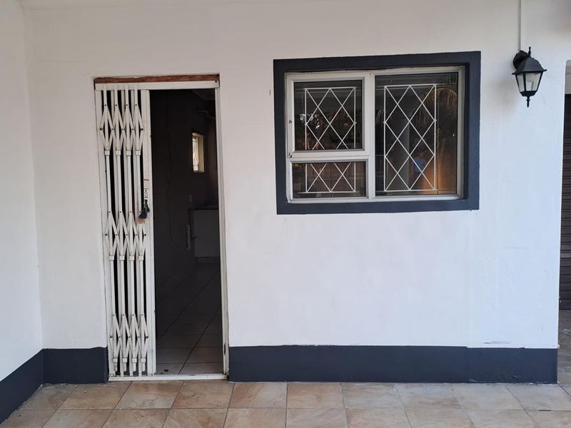A covered patio area featuring tiled flooring, a security gate entrance, and a window with security bars, providing a functional outdoor transition space.