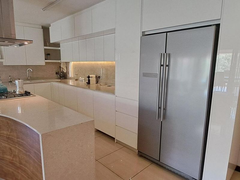 Modern kitchen featuring high-gloss white cabinetry, stone countertops, a curved breakfast bar, integrated appliances, and sleek under-cabinet lighting.