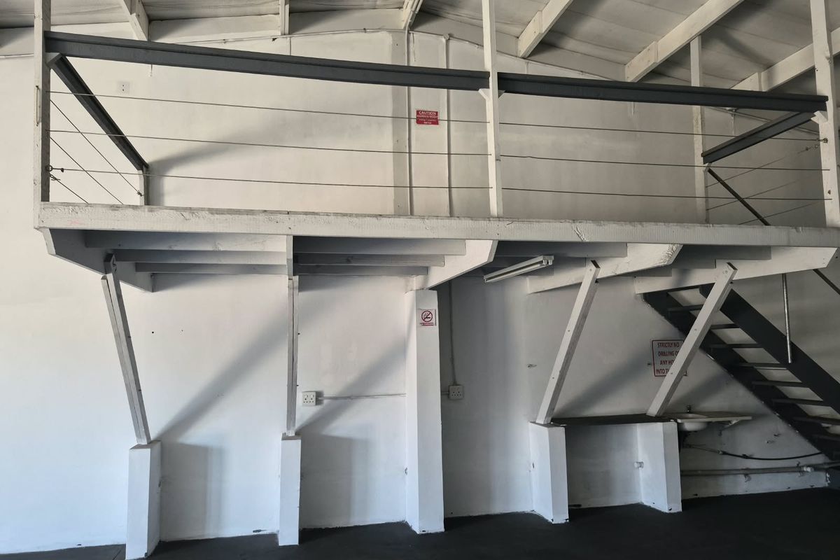 Industrial utility space featuring a mezzanine level with steel balustrades, exposed roof trusses, and a functional sink area, suitable for storage or workshop use.