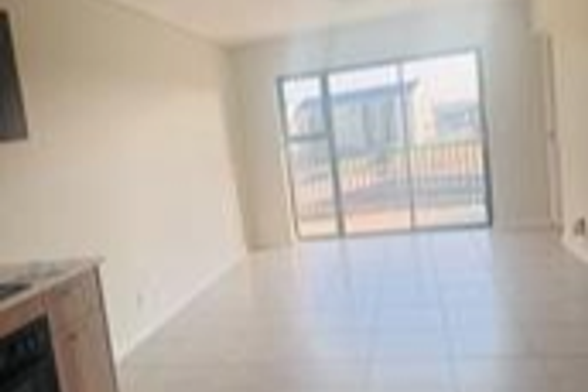 An open-plan living area featuring tiled flooring and a sliding glass door leading to a balcony, with an adjacent kitchen area.