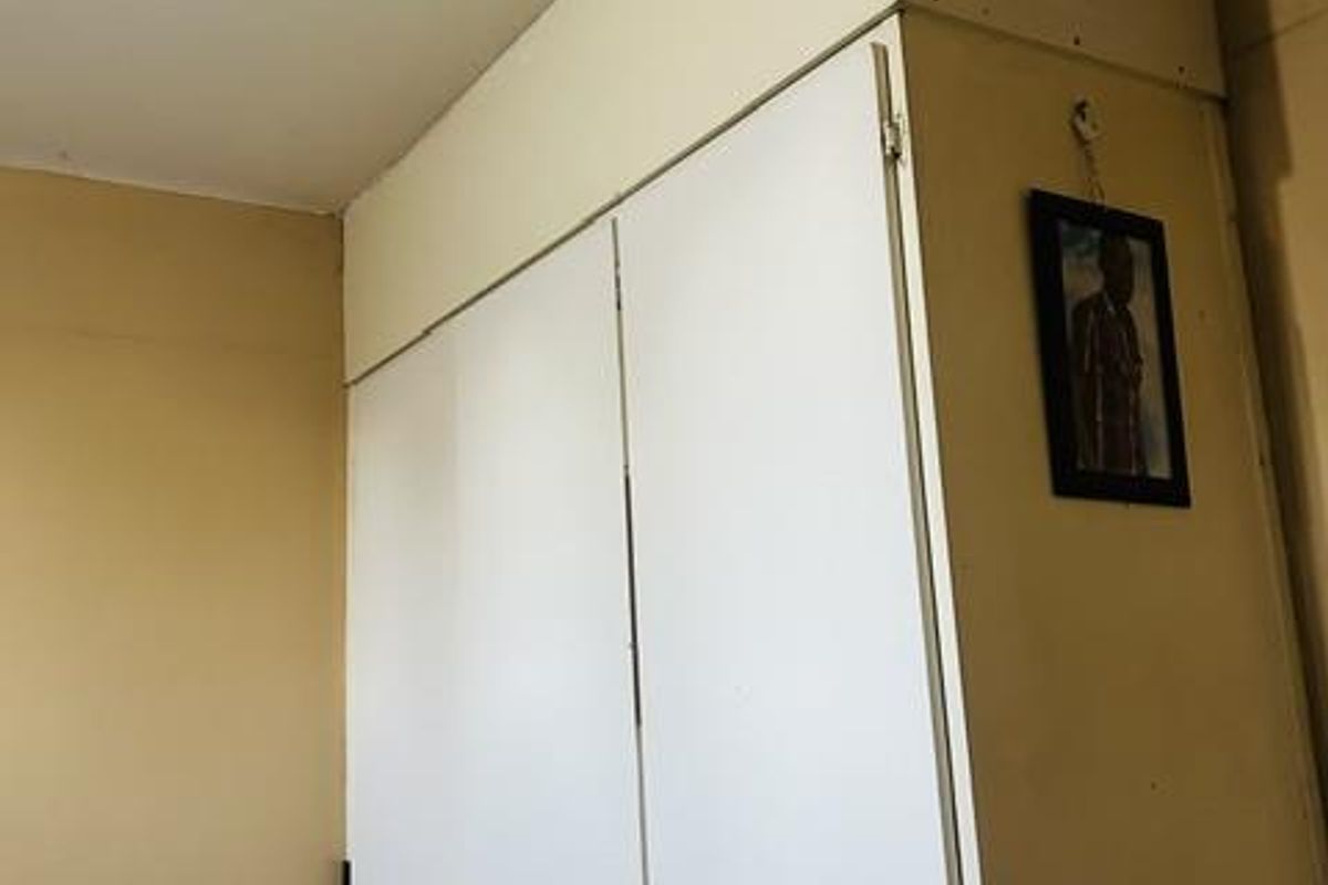 A bedroom featuring built-in floor-to-ceiling storage cupboards with white doors and overhead storage compartments.