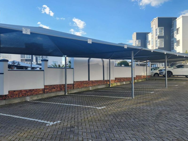 A well-maintained outdoor parking area featuring covered shade cloth carports and paved parking bays within an apartment complex.