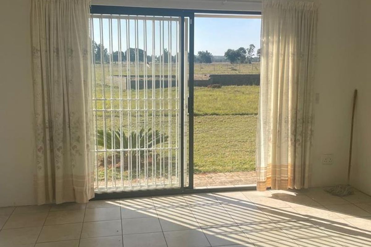 A bright living area featuring tiled flooring and a large sliding glass door with security bars, providing direct access to the garden.