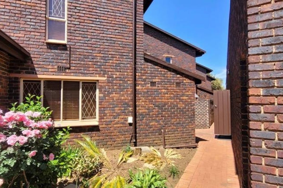 A side view of the townhouse featuring classic face brick exterior, leaded glass windows, and a paved walkway leading to the rear area.
