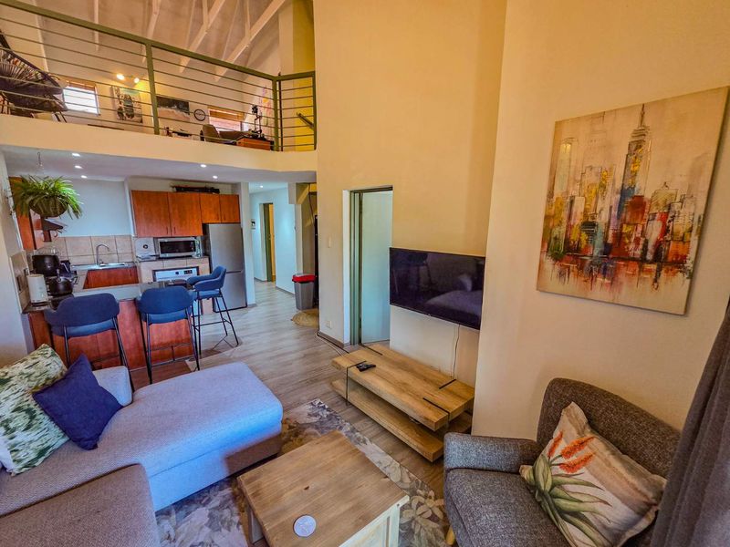 Open-plan living area featuring a kitchen with wood-finish cabinetry, a breakfast bar, and a mezzanine level with a metal balustrade overlooking the space.