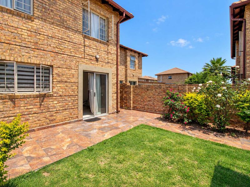 A private rear garden featuring a tiled patio area, face brick exterior walls, and a well-maintained lawn enclosed by a brick boundary wall.