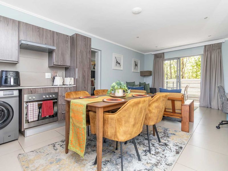 An open-plan living and kitchen area featuring modern wood-grain cabinetry, integrated appliances, tiled flooring, and direct access to an outdoor patio through sliding doors.