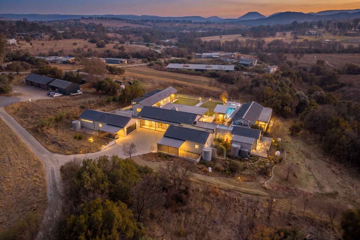 Aerial view of a modern, expansive residential property featuring multiple interconnected buildings, a swimming pool, landscaped grounds, and scenic rural surroundings at dusk.