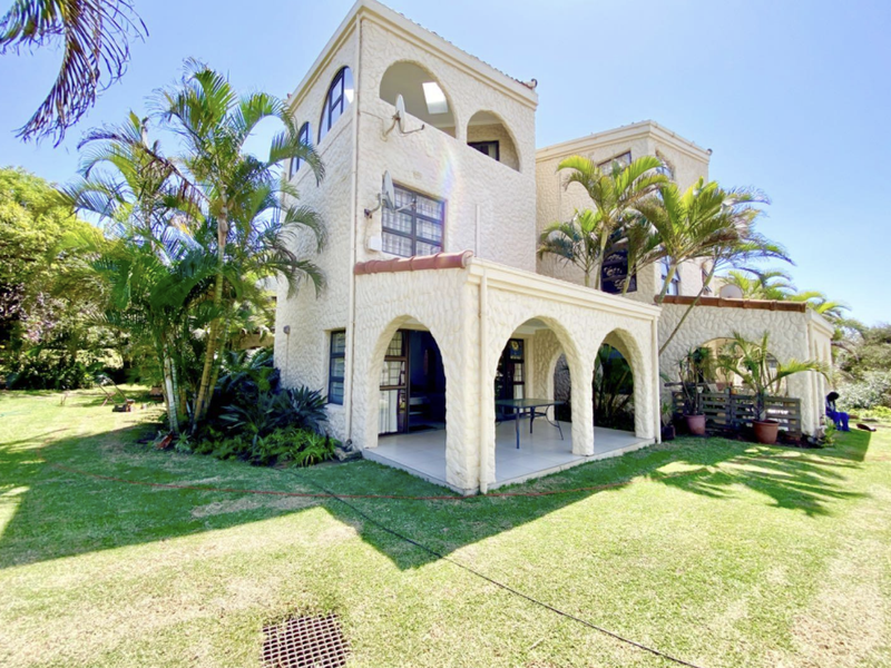 Rear view of a multi-level house featuring a covered arched patio, textured exterior walls, and a well-maintained garden area.