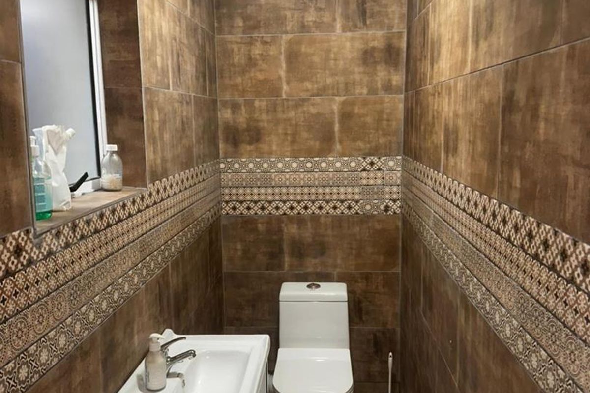 A compact guest bathroom featuring full-height brown decorative tiling, a modern vanity basin, and a dual-flush toilet.