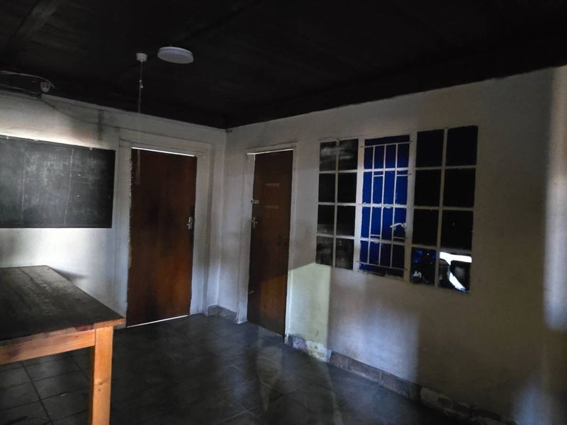A dimly lit, vacant utility space featuring tiled flooring, a dark timber ceiling, and security-barred windows, requiring cosmetic refurbishment.