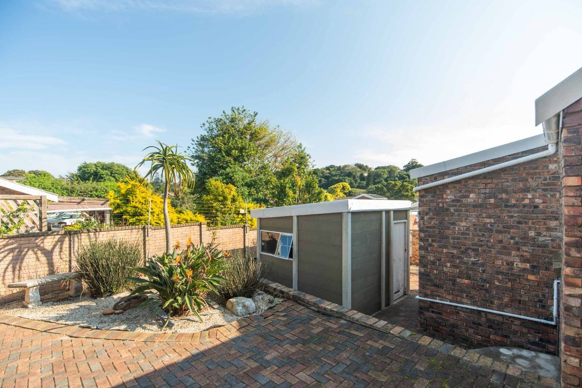 A rear garden area featuring a paved courtyard, a small detached storage shed, and established landscaping with a brick boundary wall.