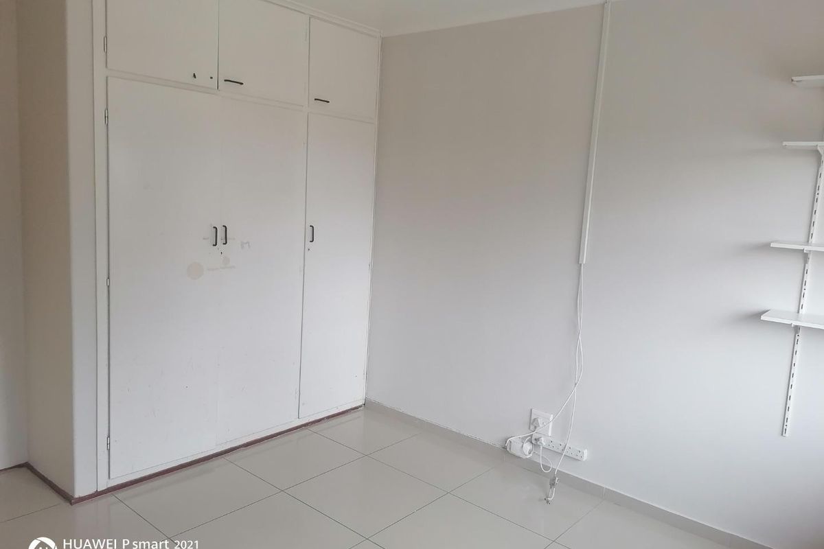 An empty bedroom featuring tiled flooring, built-in cupboards, and wall-mounted shelving units.