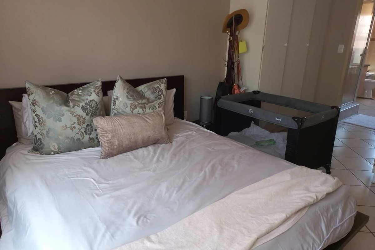 A bedroom featuring built-in cupboards and tiled flooring, with an adjoining en-suite bathroom visible in the background.