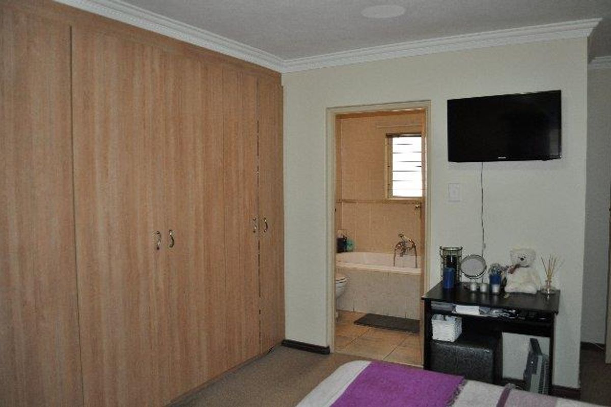 Bedroom featuring extensive built-in wooden cupboards and direct access to an en-suite bathroom with a bathtub and tiled flooring.