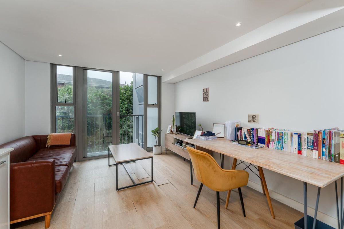 A bright living room featuring modern laminate flooring, recessed lighting, and a large sliding glass door providing access to a private balcony.