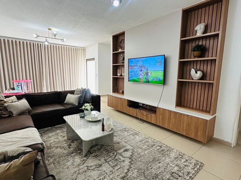 A well-maintained living room featuring a custom built-in wooden shelving unit, tiled flooring, and contemporary light fixtures.