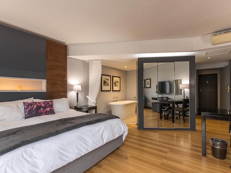 Spacious bedroom featuring a modern open-plan layout with a freestanding bathtub, mirrored wardrobe, and integrated wall lighting.